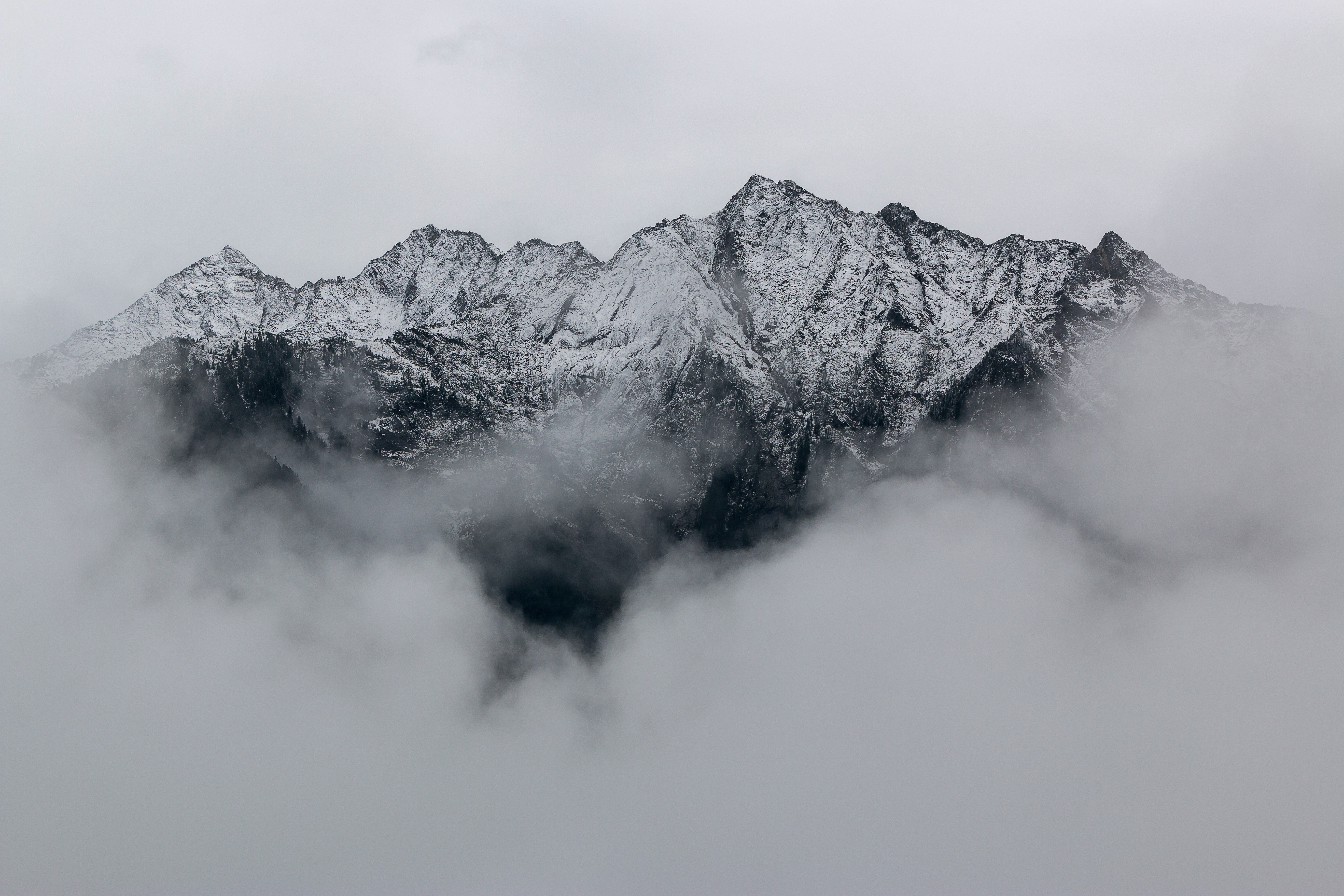 A jagged, rocky, mountainous skyline emerging from clouds with grey sky behind.